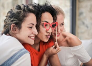 Three women enjoying a playful moment with heart-shaped glasses, symbolizing friendship and fun.