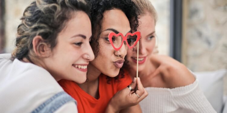 Three women enjoying a playful moment with heart-shaped glasses, symbolizing friendship and fun.